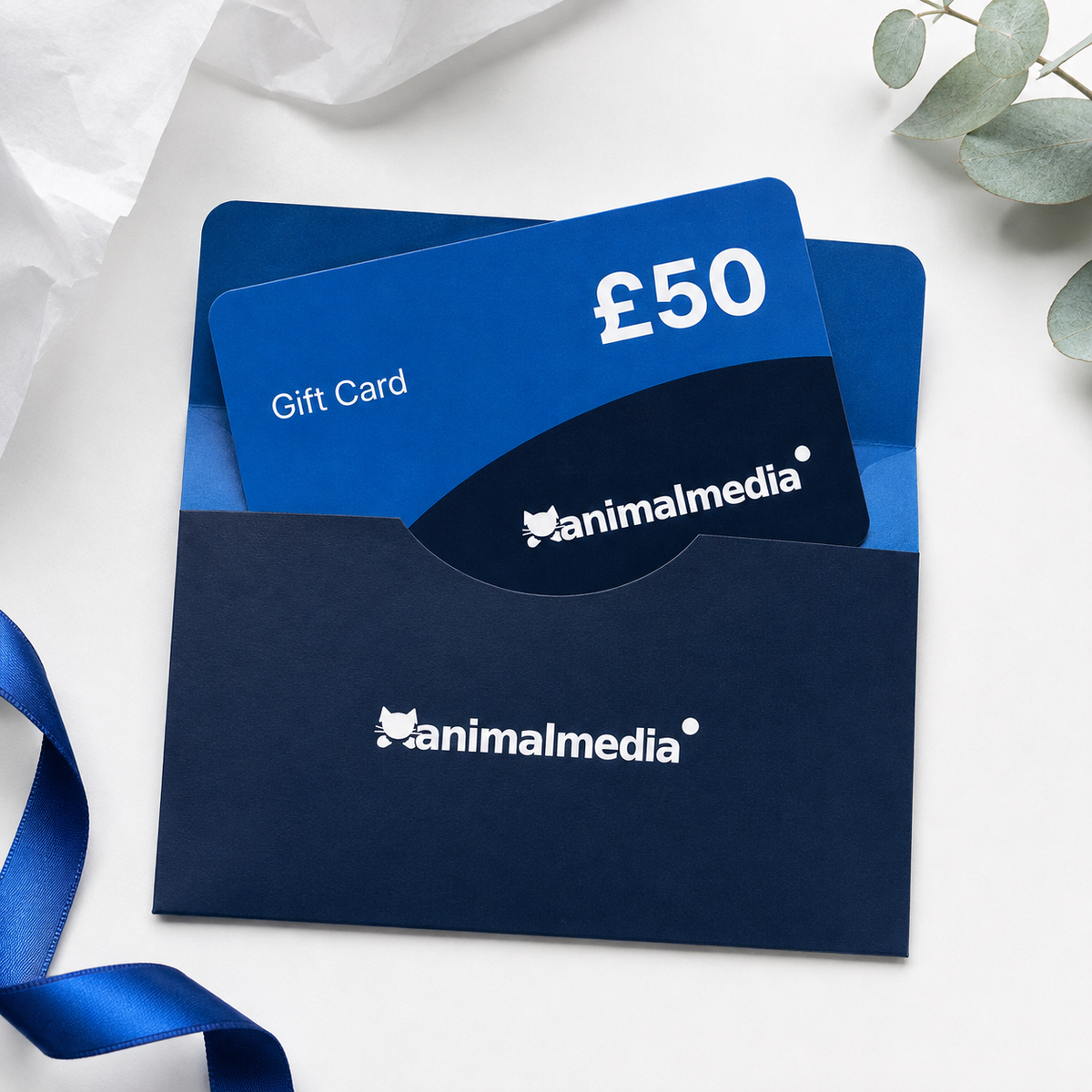 A blue and navy Animalmedia gift card set with a matching envelope, styled on a white surface with a blue ribbon and eucalyptus leaves.
