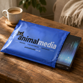A blue Animalmedia branded mailer envelope and a dark collectible box rest on a rustic wooden table, with a coffee cup and home interior softly blurred in the background.