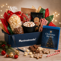 A Christmas-themed gift box set from animalmedia, featuring a navy blue box filled with popcorn, candy canes, marshmallows, gingerbread cookies, and a 'Christmas Blu Ray' box, arranged on a wooden surface with festive decorations and warm string lights in the background.