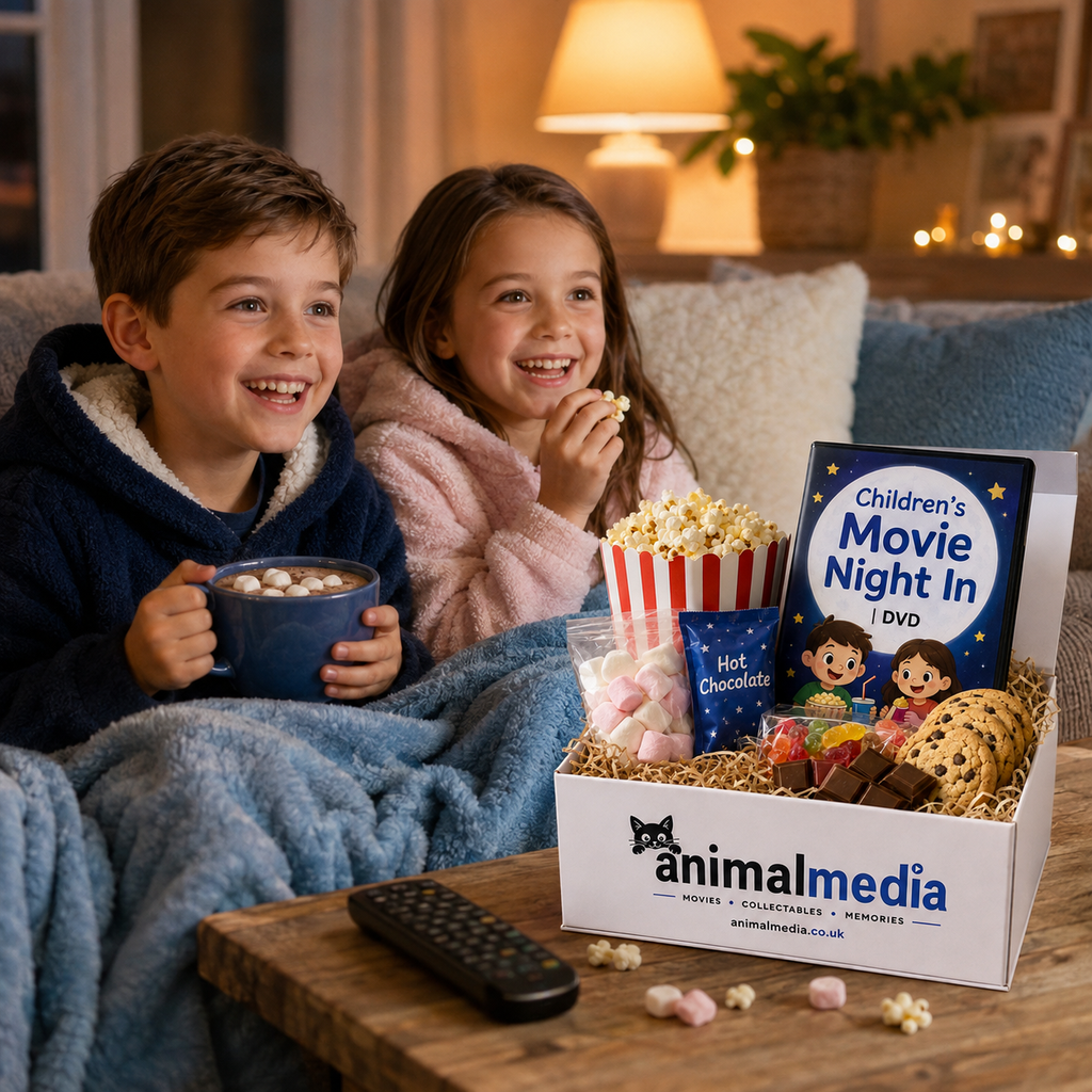 A cozy living room scene with two children in plush robes sitting on a couch under a lamp, smiling while watching a DVD. In front of them is an Animal Media gift box filled with popcorn, marshmallows, chocolate, cookies, and a remote, with a book titled "Children's Movie Night In DVD" standing in the box.