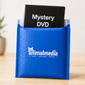 A blue bubble mailer envelope with the white 'animalmedia' logo on the front, holding a black DVD case that reads 'Mystery DVD' in white text, set on a light wood surface against a soft beige background.