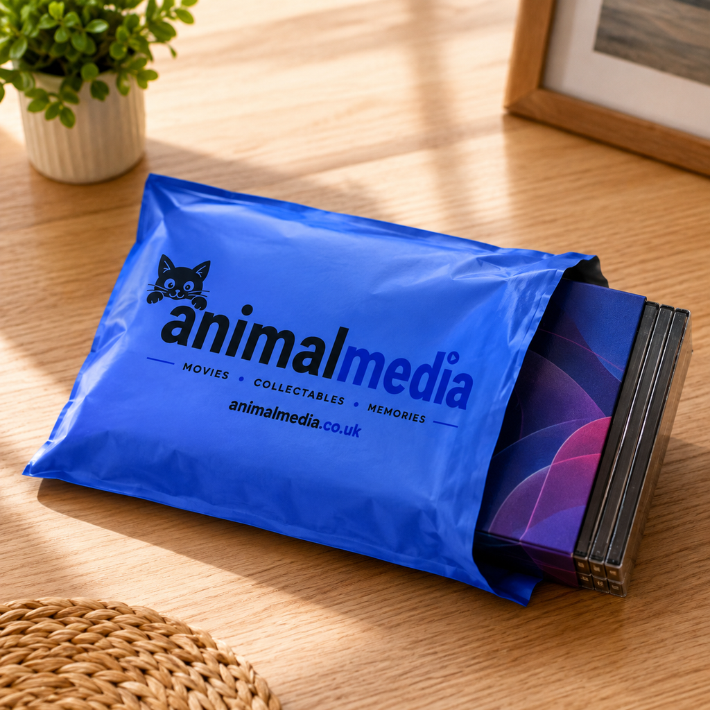 A blue Animalmedia branded mailer envelope containing a stack of collectible cards, placed on a wooden table with a small plant and framed picture in the background.